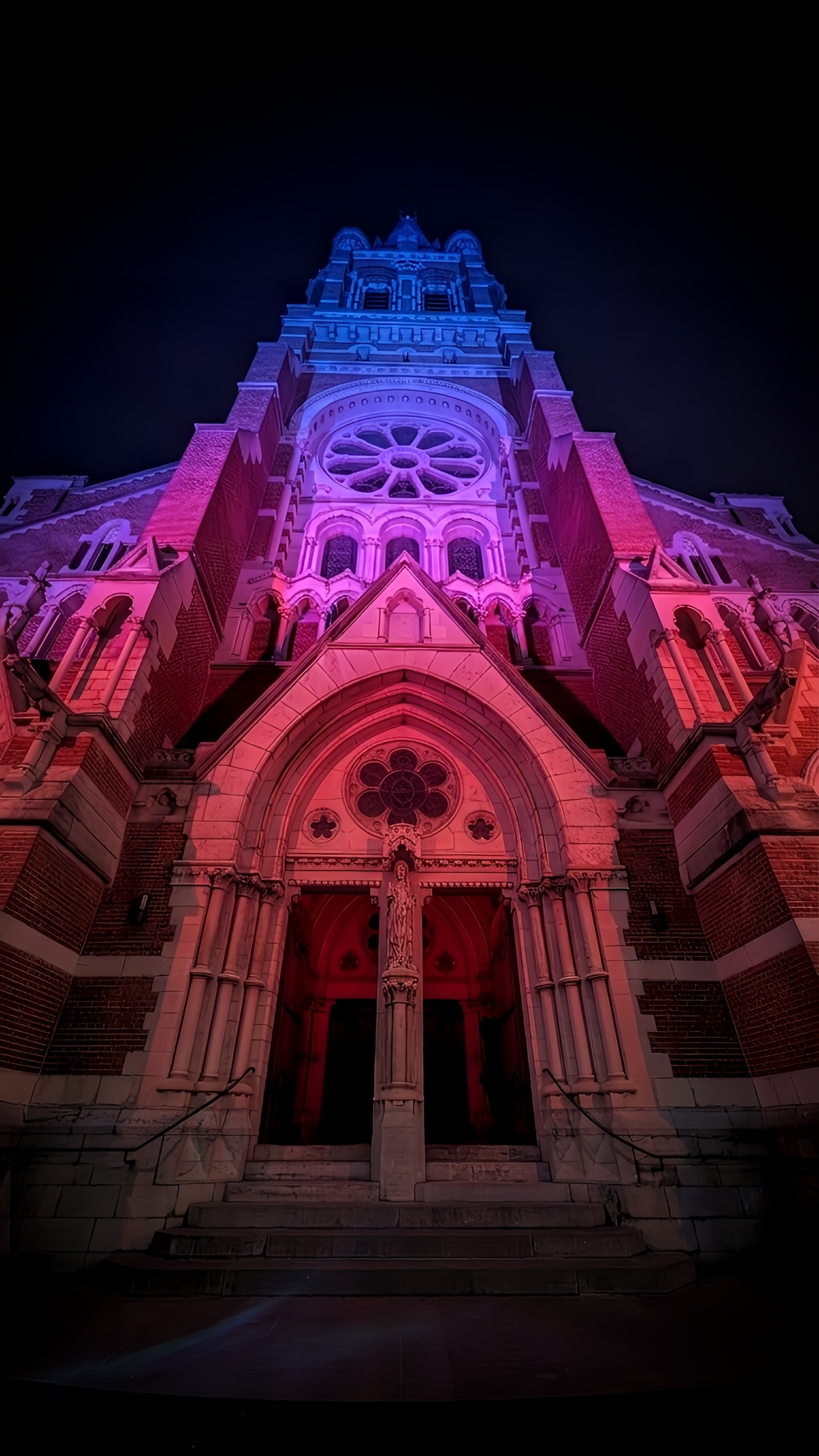 Exterior church tower at night illuminated in red, pink, purple and blue gradient lights
